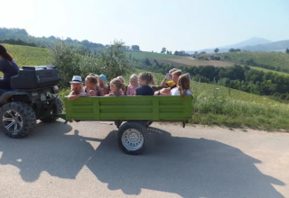 Niños viajan en un remolque verde tirado por un ATV por las colinas de Agricampeggio Tasteria en Marche, Italia.