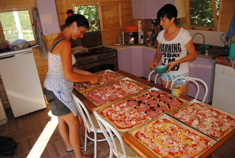 Zwei Frauen bereiten große Bleche Pizza in einer gemütlichen Küche im Agricampeggio Tasteria, Marche, Italien zu.