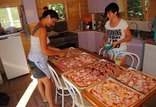 Two women prepare large trays of pizza in a cozy kitchen at Agricampeggio Tasteria, Marche, Italy.