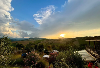 Zonsondergang boven de heuvels bij Agricampeggio Tasteria, een vakantiepark in Marche, Italië, met bloemen.