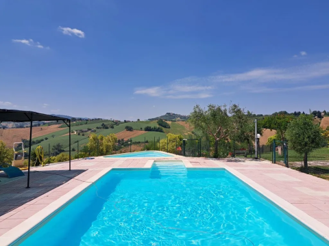 Vista de la piscina en Agricampeggio Tasteria, un parque vacacional en Marche, Italia, con colinas al fondo.