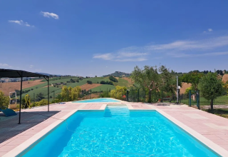 Vista sulla piscina di Agricampeggio Tasteria, parco vacanze nelle Marche, Italia, con colline sullo sfondo.