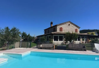 Stone house with pool and loungers under a clear sky at Agricampeggio Tasteria, Marche, Italy.