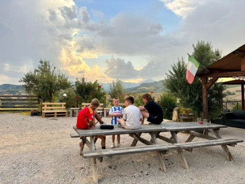 Children sit on a picnic bench at Agricampeggio Tasteria holiday park in Marche, Italy, with mountains view.