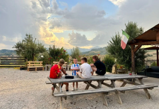Kinder sitzen an einem Tisch im Agricampeggio Tasteria Ferienpark in Marche, Italien, bei Sonnenuntergang.