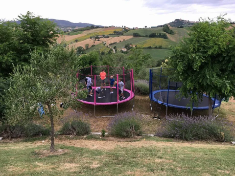 Kinderen spelen op twee trampolines in een tuin met uitzicht over de heuvels van Marche, Italië.
