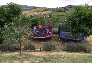 Kinderen spelen op twee trampolines in een tuin met uitzicht over de heuvels van Marche, Italië.
