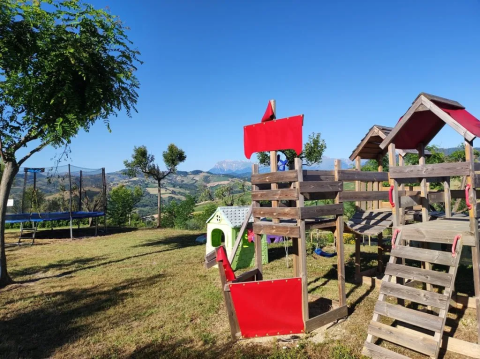 Legeplads og trampolin ved Agricampeggio Tasteria i Marche, Italien, med smukke bjerge i baggrunden.