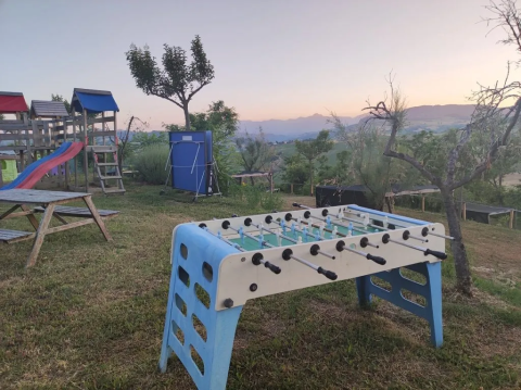 Udsigt over en legeplads med bordfodboldbord og gynger på en græsmark ved Agricampeggio Tasteria i Marche, Italien.