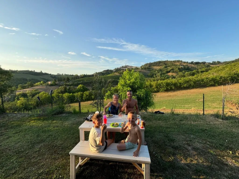 Eine Familie isst draußen an einem Tisch mit Blick auf die Hügel von Agricampeggio Tasteria in Marche, Italien.