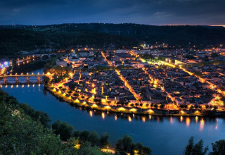 Luftfoto af en smuk, oplyst by ved en flod omkring Montcléra, Occitanie, Frankrig, taget ved skumring.
