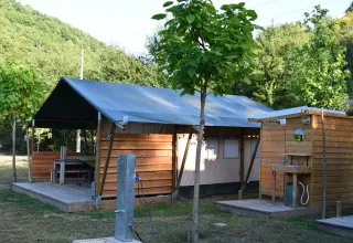 Safaritent op een camping met houten terras, buitenkeuken en groene heuvels als achtergrond.