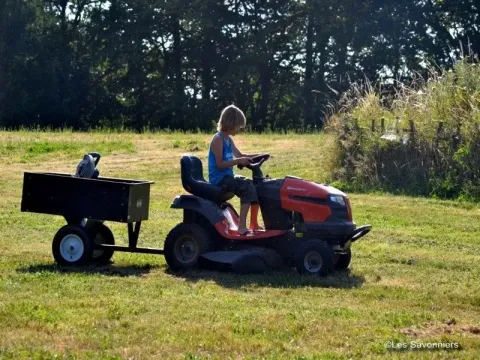 Child driving a lawn tractor with a trailer in a sunny park at Les Savonniers, Occitanie, France.