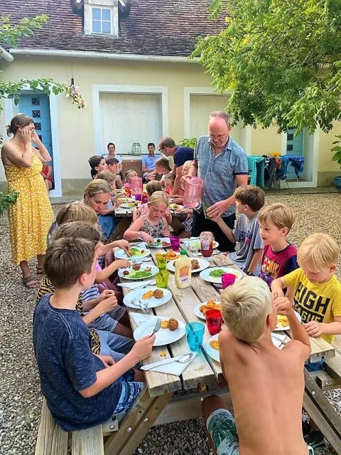 Sommermiddag med børn og voksne, der nyder et måltid sammen udendørs på Les Savonniers i Occitanie, Frankrig.