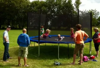 Kinder springen auf einem Trampolin mit Erwachsenen im Ferienpark 'Les Savonniers', Occitanie, Frankreich.