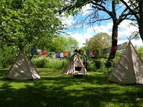 Tres tipis y banderas de colores en Les Savonniers, un parque vacacional en Occitanie, Francia, rodeados de árboles.