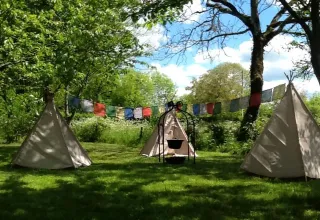 Drie tipi’s met kleurrijke vlaggetjes in Les Savonniers vakantiepark, Occitanië, Frankrijk, tussen bomen.