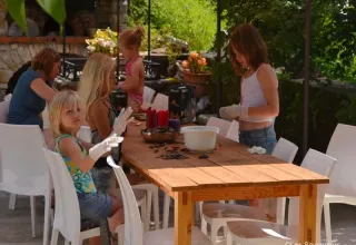 Bambini e adulti svolgono attività a un tavolo all'aperto al parco vacanze Les Savonniers in Occitania, Francia.