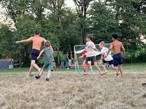 Børn og voksne spiller fodbold på en græsplæne i ferieparken Les Savonniers i Occitanie, Frankrig.