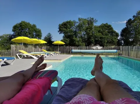 Personas relajándose en tumbonas junto a una piscina con paraguas amarillos en Les Savonniers, Occitanie, Francia.