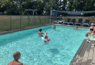 Families enjoy a sunny day swimming at Les Savonniers holiday park pool in Occitanie, France, with loungers nearby.
