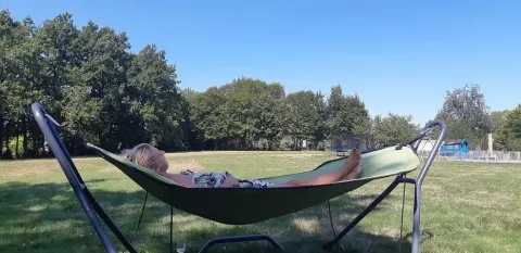 Vrouw rustend in een hangmat aan de Safaritent bij Les Savonniers in Frankrijk, met bomen en groene velden.
