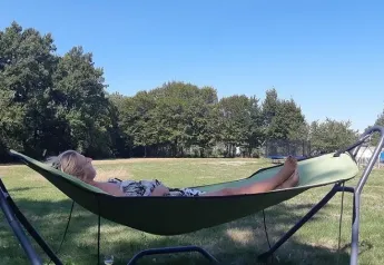 Vrouw rustend in een hangmat aan de Safaritent bij Les Savonniers in Frankrijk, met bomen en groene velden.