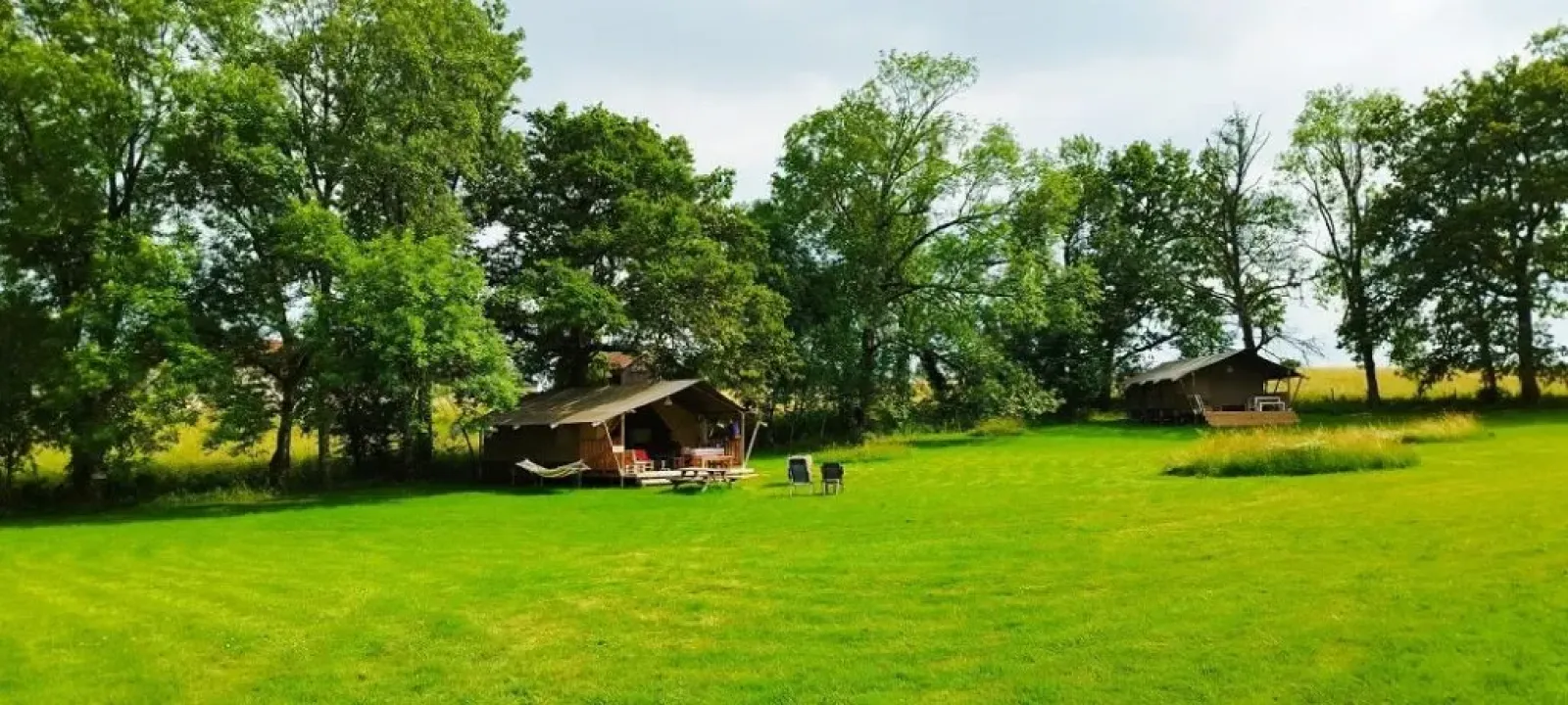 Groen grasveld met twee safaritenten onder hoge bomen bij Les Savonniers in Frankrijk, perfect voor rust.