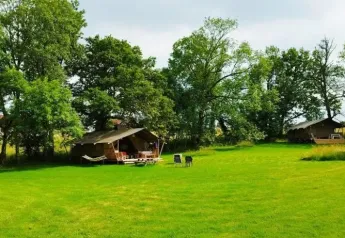 Uitgestrekt groen veld met twee safaritenten tussen bomen bij Les Savonniers in Frankrijk, ideaal om te ontspannen.