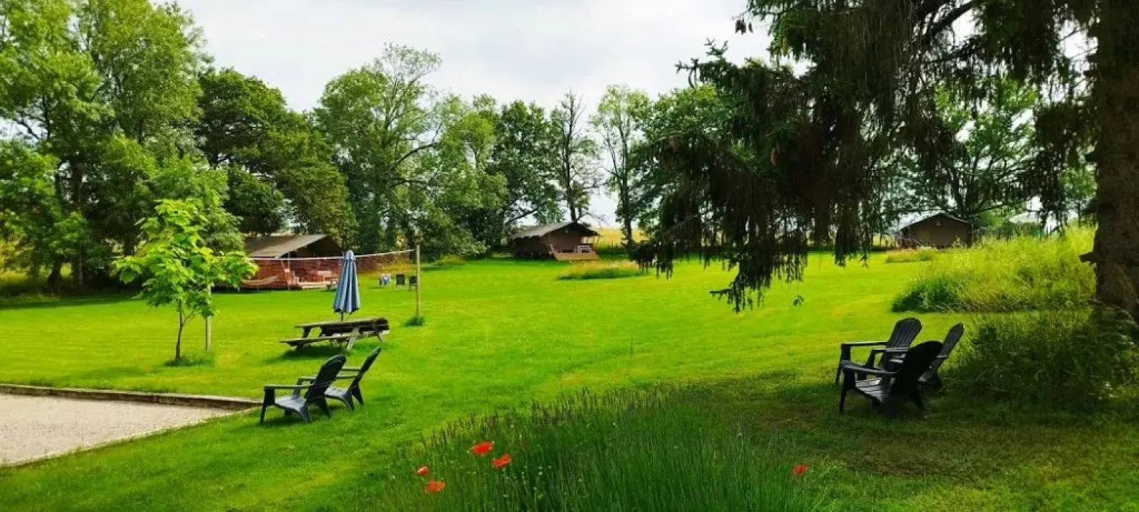 Groen kampeerterrein met safaritenten, bomen en stoelen buiten bij Les Savonniers in Frankrijk.