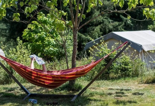 Person liest in einer Hängematte bei Safaritent met badkamer auf Camping La Bretonniere, Frankreich, inmitten der Natur.