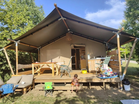 Safari-Zelt mit Holzterrasse und Kinderspielzeug vor Camping La Bretonniere in Frankreich bei Sonne.