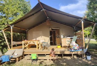 Safari-Zelt mit Holzterrasse und Kinderspielzeug vor Camping La Bretonniere in Frankreich bei Sonne.