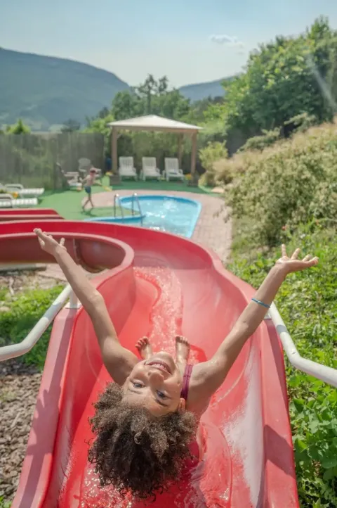 Kind in badkleding glijdt lachend van een rode glijbaan bij Domaine Les 2 Soleils vakantiepark in Frankrijk.