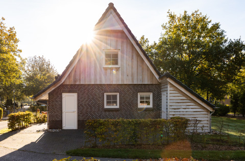 Wellness Lodge XXL aan Hof van Salland in Nederland met zonlicht en omringd door bomen en groene struiken.