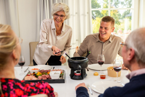 Cuatro personas disfrutan fondue en una mesa bajo luz natural durante su estancia de glamping, sonriendo alegres.