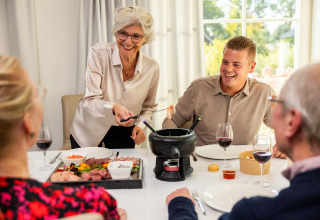 Vier Personen genießen zusammen Fondue bei natürlichem Licht in einer Glamping-Unterkunft, fröhlich am Tisch.