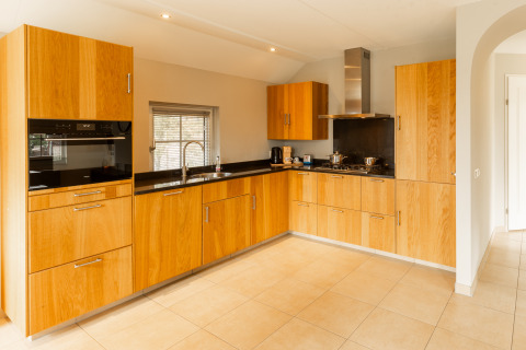 Moderne keuken met houten kasten, zwarte werkbladen en gaskookplaat in Wellness Lodge XXL bij Hof van Salland.