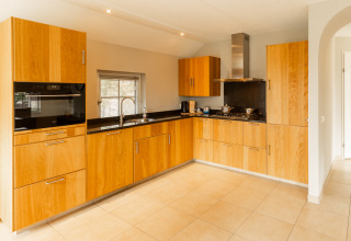 Moderne keuken met houten kasten, zwarte werkbladen en gaskookplaat in Wellness Lodge XXL bij Hof van Salland.