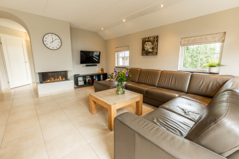 Heldere woonkamer van Wellness Lodge XXL in Hof van Salland, Nederland, met hoekzetel en open haard.