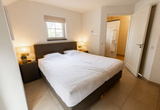 Slaapkamer in Wellness Lodge XXL bij Hof van Salland, Nederland, met tweepersoonsbed en open badkamer.