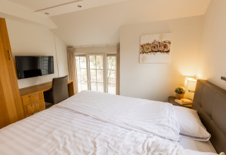 Slaapkamer in Wellness Lodge XXL van Hof van Salland, Nederland, met groot bed, televisie en bureau.