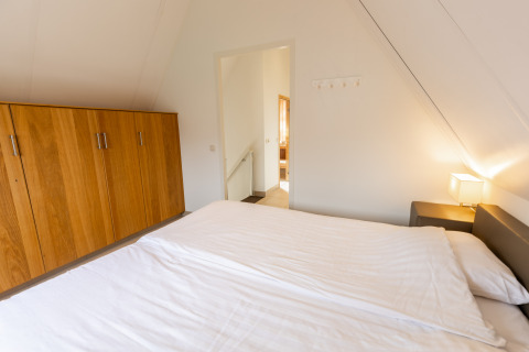 Slaapkamer met tweepersoonsbed, houten kleerkast en nachtlamp in Wellness Lodge XXL te Hof van Salland, Nederland.