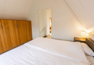 Slaapkamer met tweepersoonsbed, houten kleerkast en nachtlamp in Wellness Lodge XXL te Hof van Salland, Nederland.