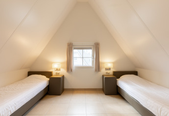 Habitación con dos camas individuales, techo inclinado y ventana en Wellness Lodge XXL, Hof van Salland, Países Bajos.