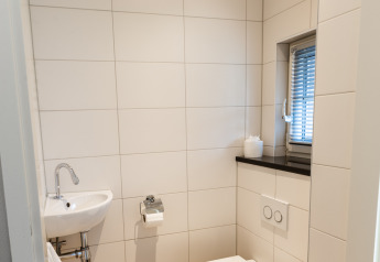 Baño moderno con inodoro suspendido, lavabo pequeño y ventana en Wellness Lodge XXL, Hof van Salland.