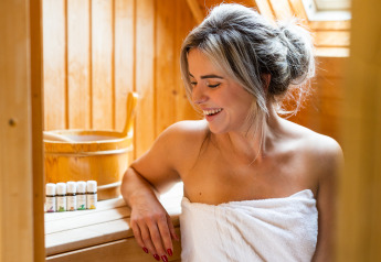 Mujer relajándose en Wellness Lodge XXL en Hof van Salland, Países Bajos, envuelta en toalla blanca en sauna.