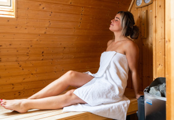 Femme se relaxant dans un sauna en bois lors d’un séjour glamping, enveloppée dans une serviette blanche.