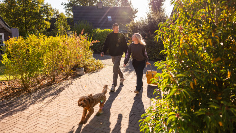 Koppel wandelt hand in hand met hond op zonnig pad bij Wellness Lodge XXL, Hof van Salland, Nederland.