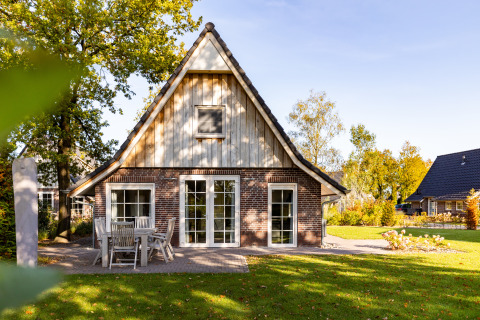 Wellness Lodge XL, una pequeña casa con fachada de ladrillo y madera, mesa al aire libre y césped verde.